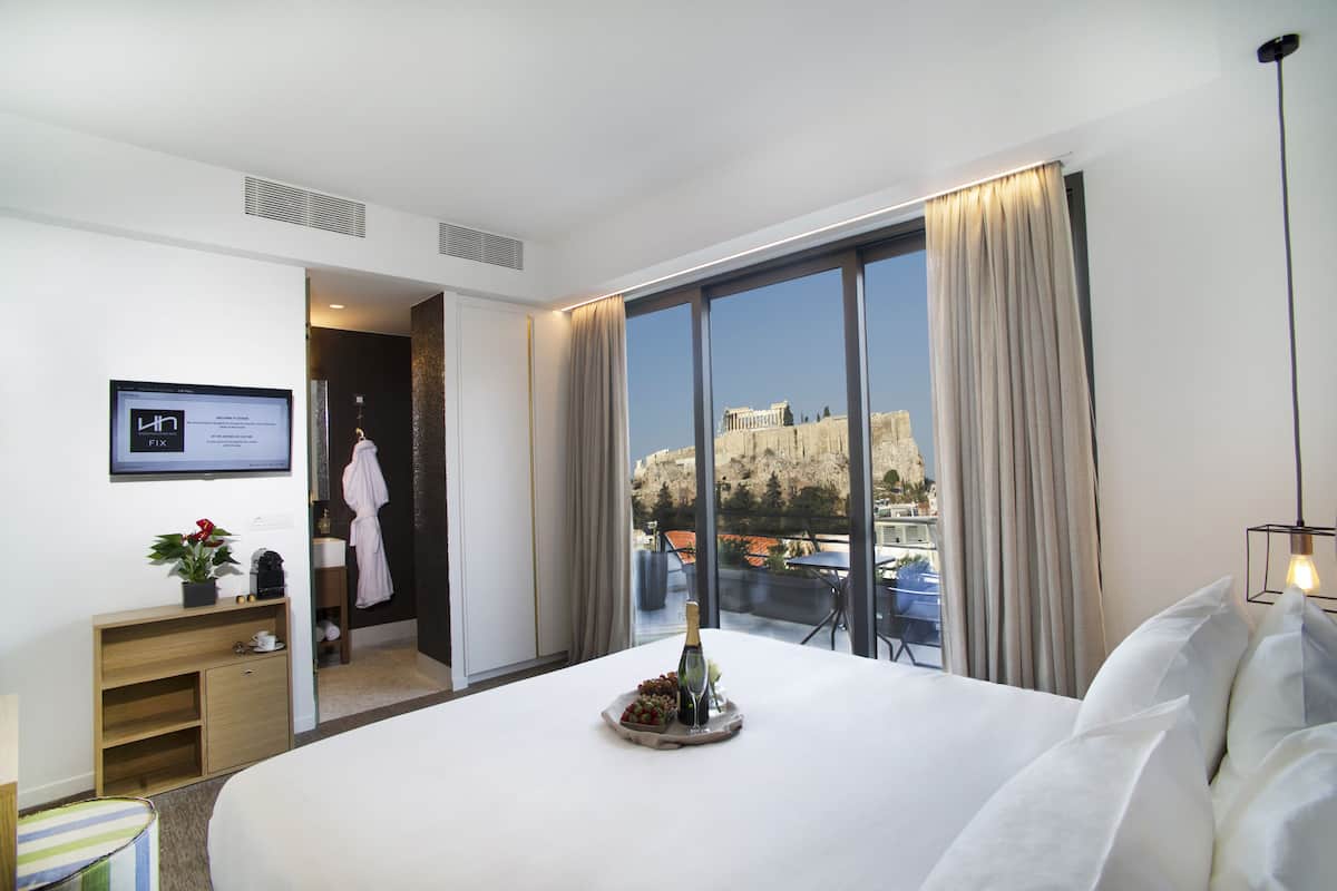 A hotel room with a large bed, a desk with a computer, a small plant, and a view of a historic building.