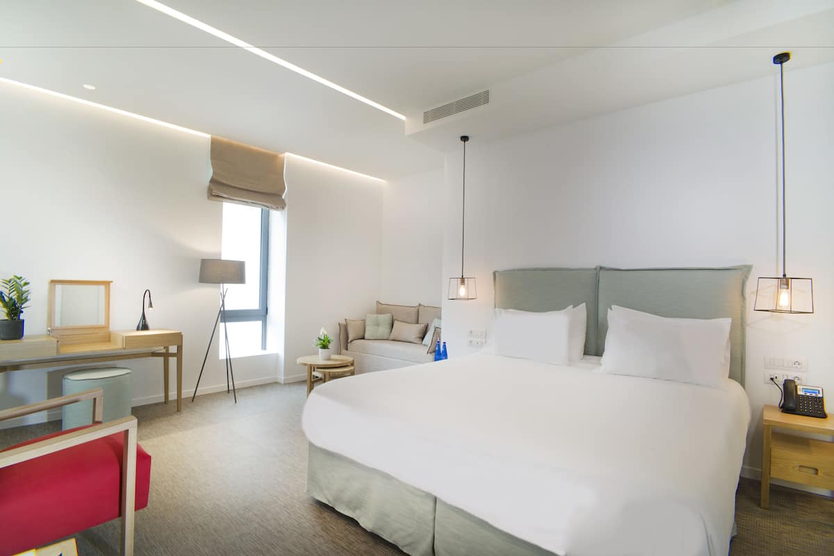 A hotel room with a large bed, bedside tables, a desk, a chair, and a window with a view.