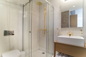 Uma casa de banho moderna com chuveiro envidraçado, lavatório branco e toucador de madeira.