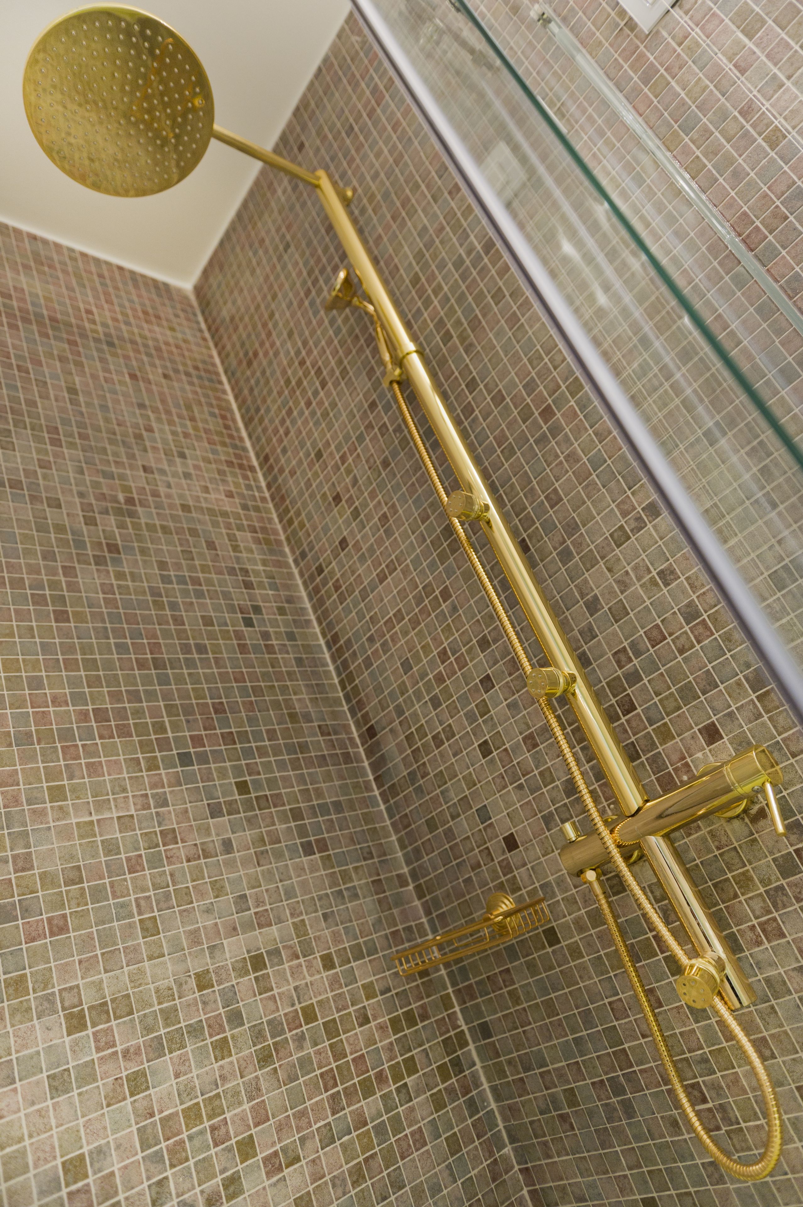 A shower with a gold showerhead and a glass enclosure.