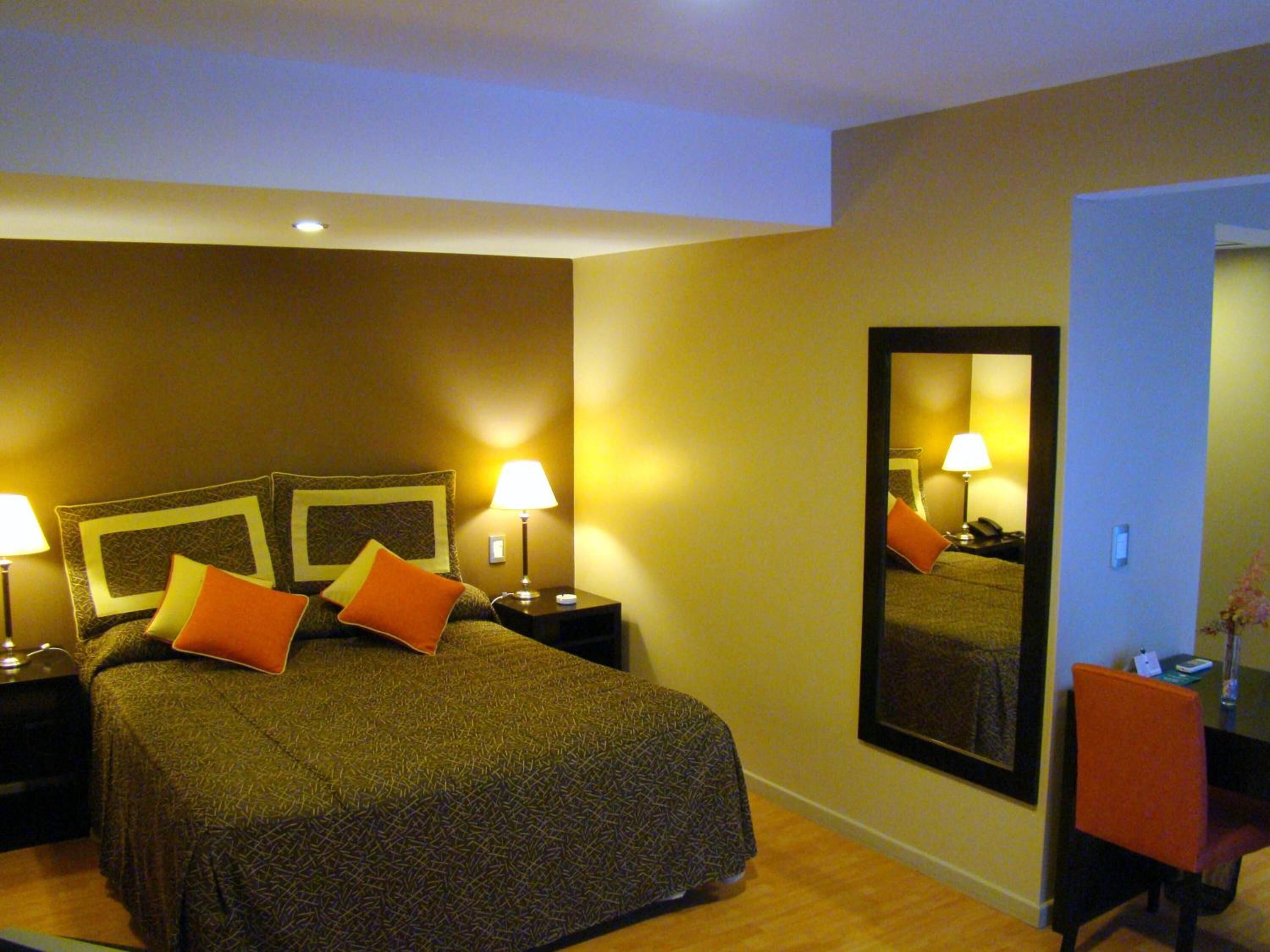 A hotel room with a large bed, two bedside lamps, a mirror, and a desk with a chair.