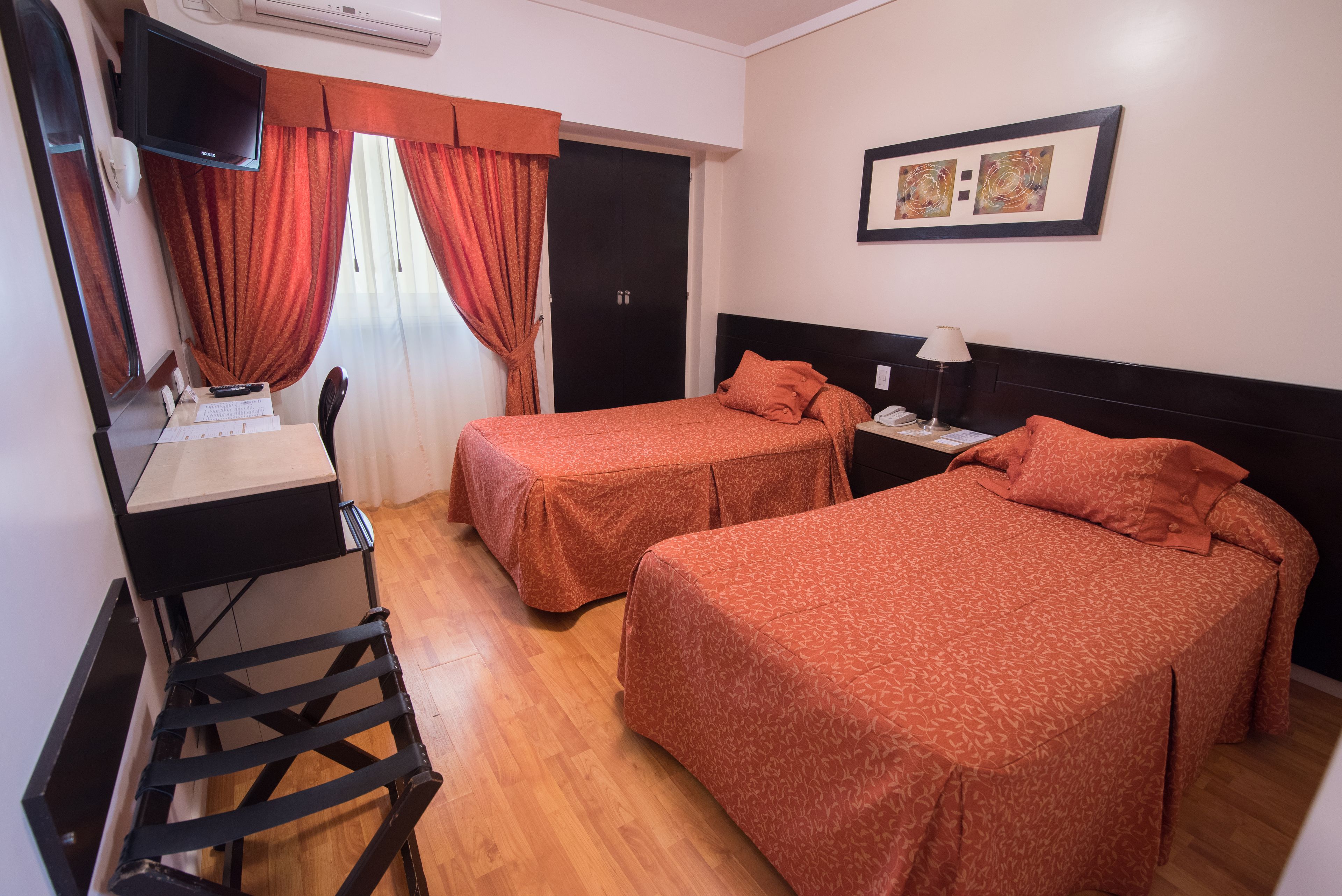 A hotel room with two beds, a desk with a chair, a TV, and a window with curtains.