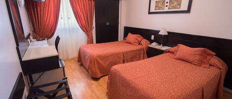 Habitación de hotel con dos camas, un escritorio con silla, televisión y ventana con cortinas.