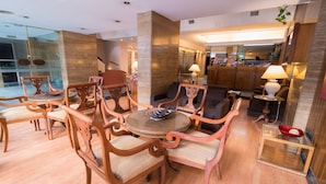 A spacious lobby with a round wooden table surrounded by ornate chairs, a glass partition, and a reception area in the background. - Gran Hotel Continental (Mar del Plata)