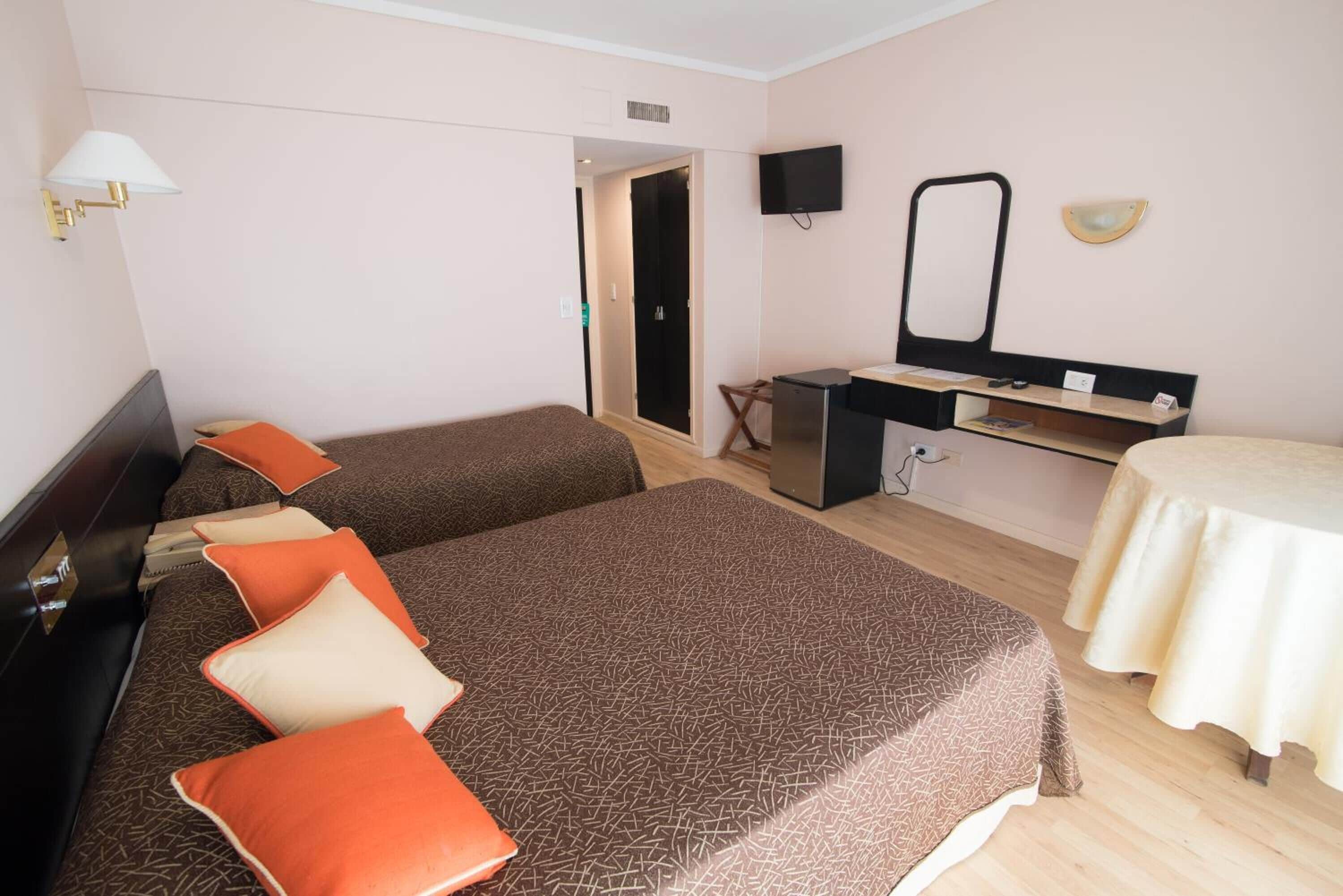 A hotel room with two beds, a desk, a chair, a TV, and a mirror.