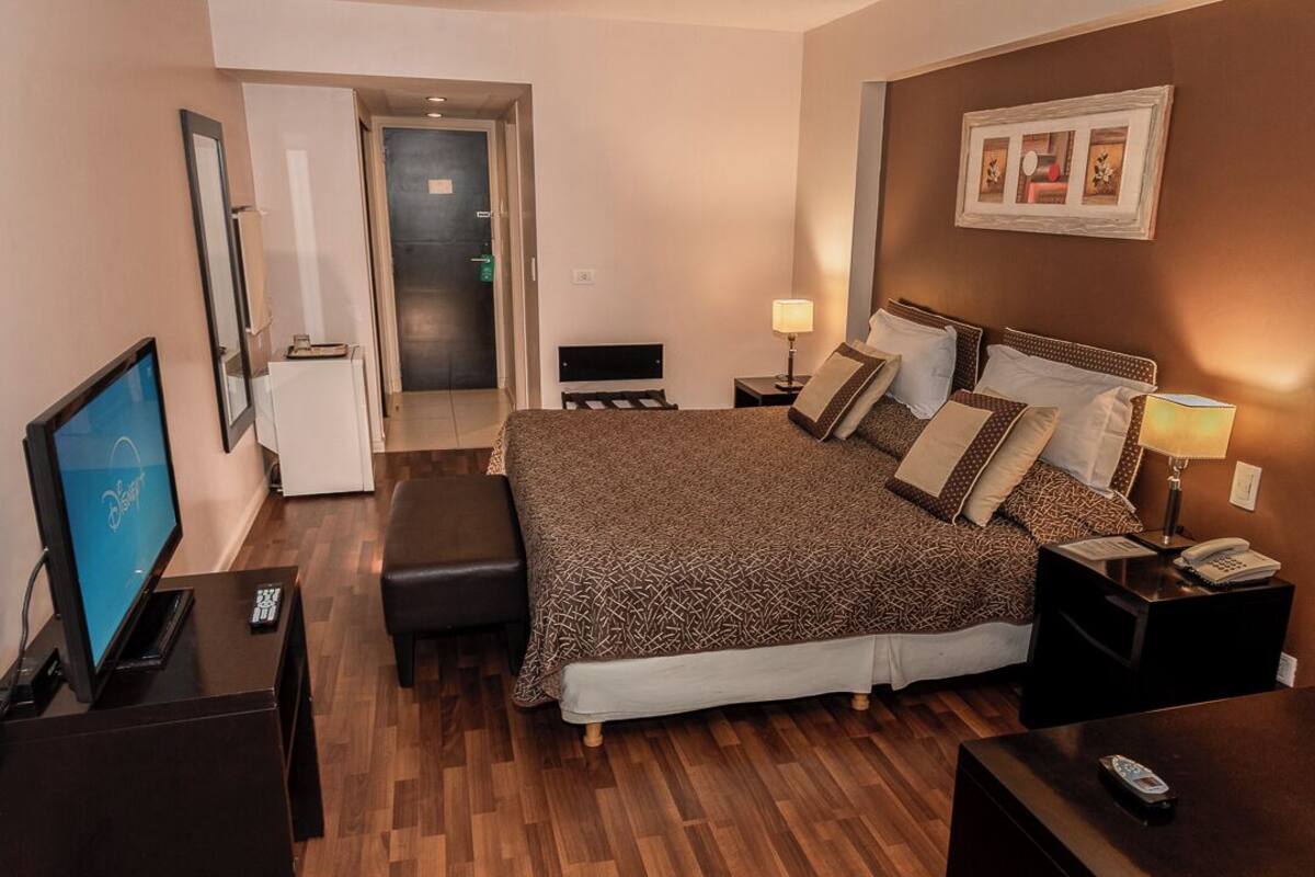 Habitación de hotel con una cama grande, un escritorio con una computadora, un televisor y una puerta que da a un baño.