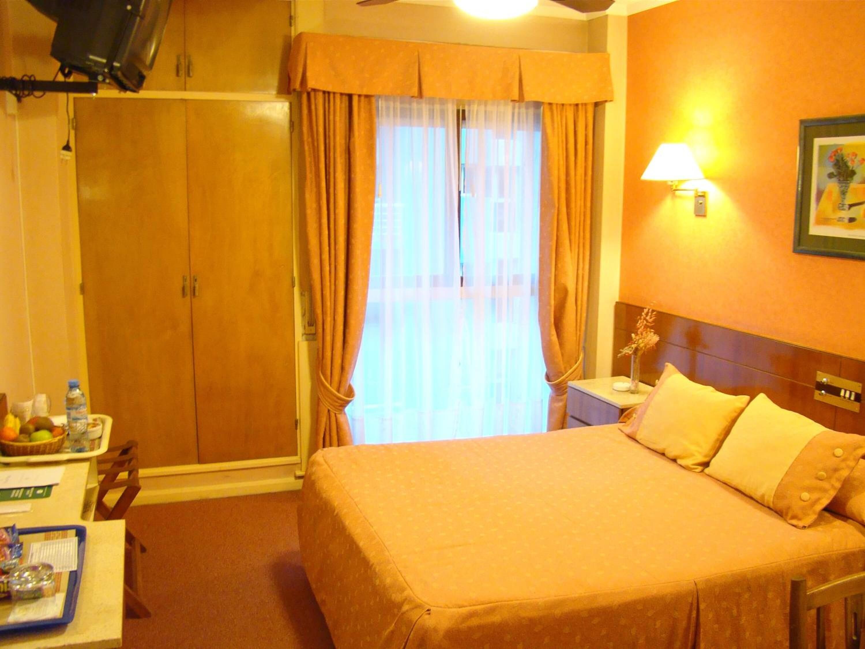 A hotel room with a bed, a nightstand, a lamp, a picture on the wall, and a wardrobe.