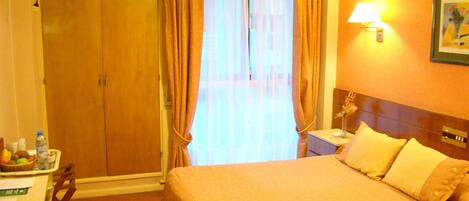 Una habitación de hotel con cama, mesita de noche, lámpara, un cuadro en la pared y armario.