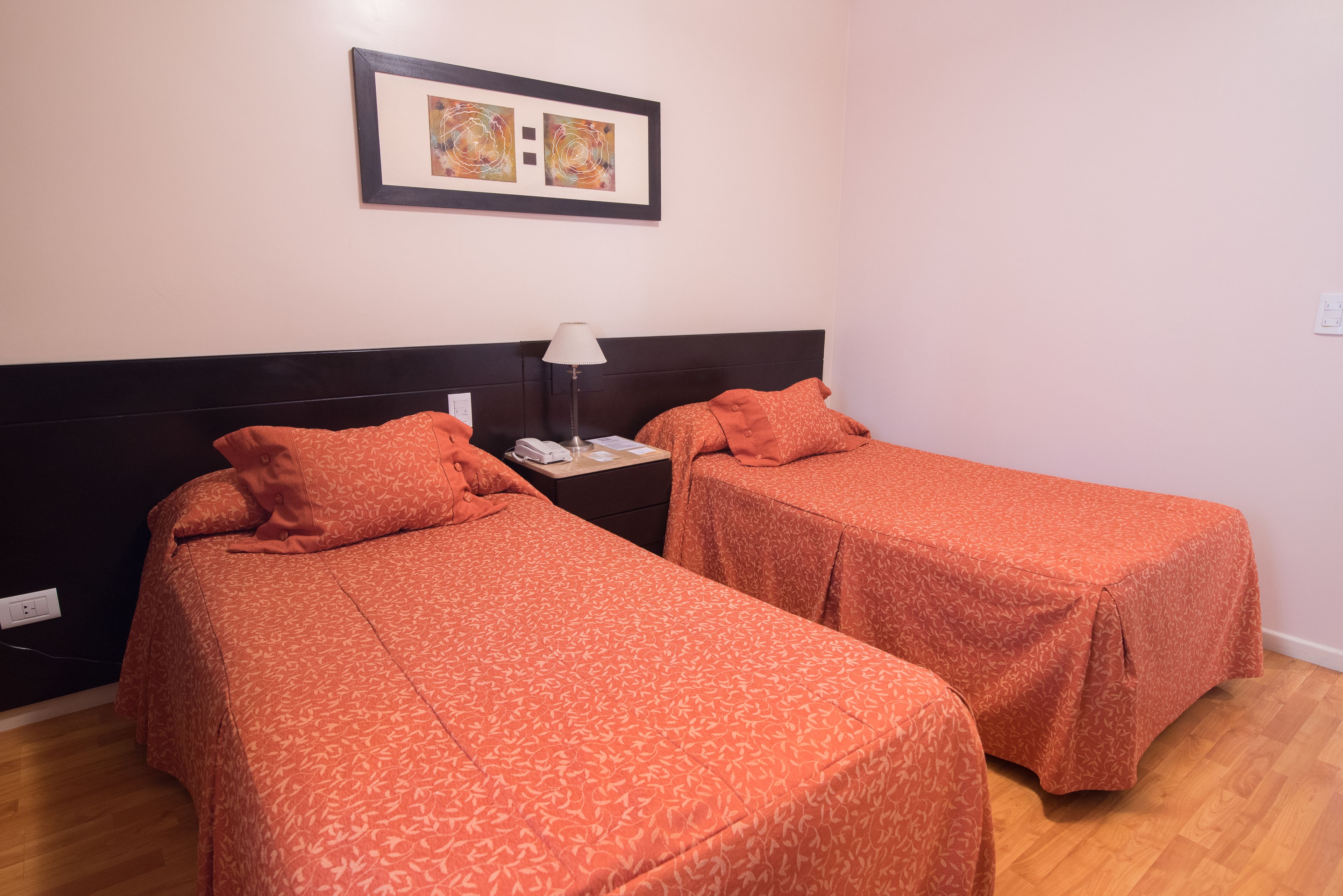 A room with two single beds, a nightstand with a lamp, and a framed artwork on the wall.