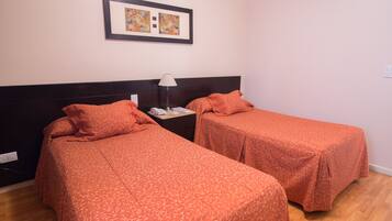 A room with two single beds, a nightstand with a lamp, and a framed artwork on the wall.