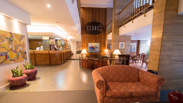 A hotel lobby with a reception desk, a sofa, potted plants, and a staircase. - Gran Hotel Continental (Mar del Plata)