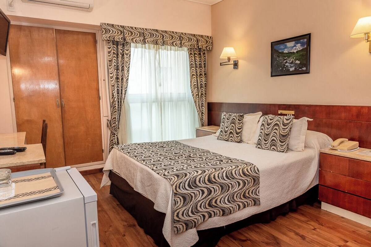 Una habitación de hotel con una cama, mesita de noche, lámpara y un cuadro en la pared.
