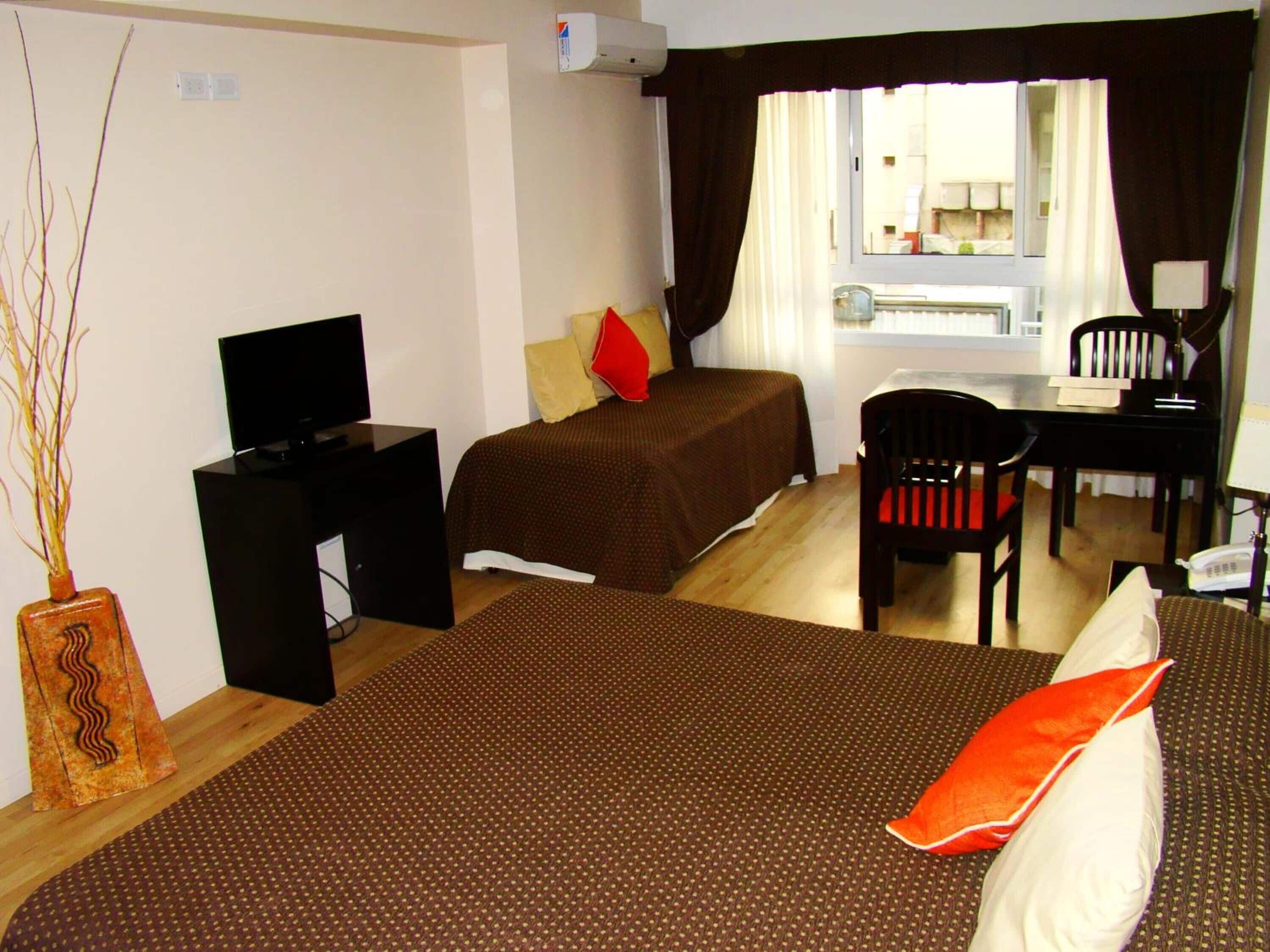 A hotel room with two beds, a desk, a chair, a television, and a window with curtains.