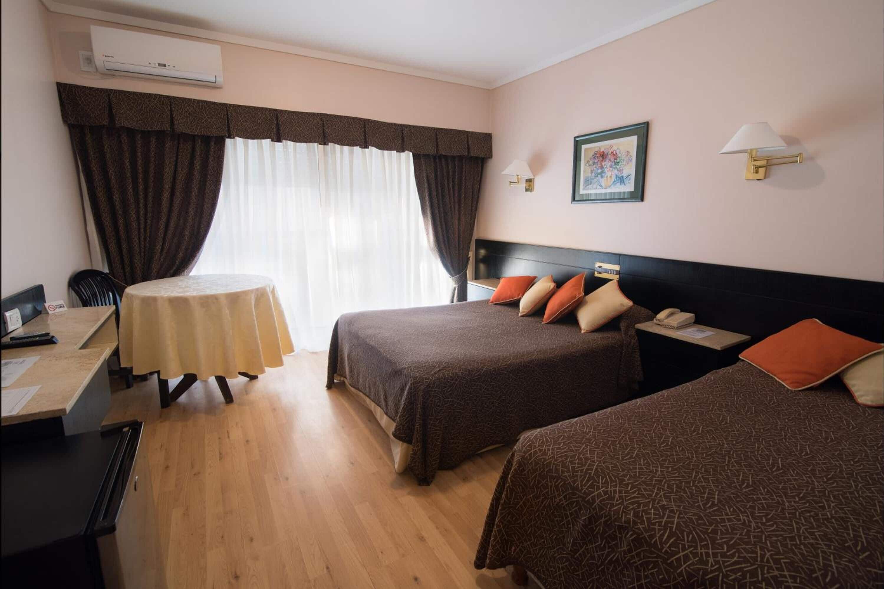 A hotel room with two beds, a desk, a chair, a table, and a wall-mounted phone.