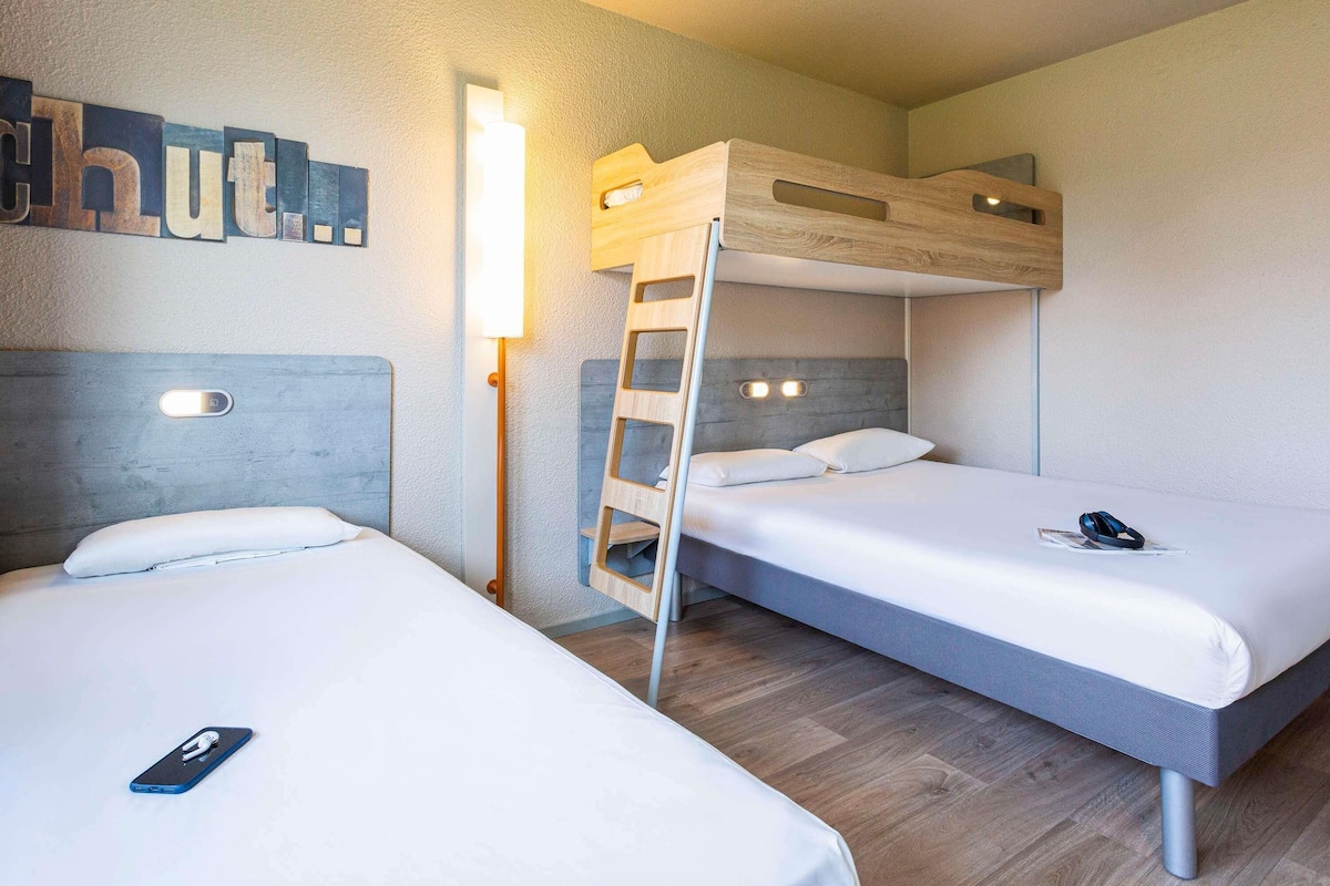 A bunk bed room with a ladder, a bedside table, and a wall-mounted light.