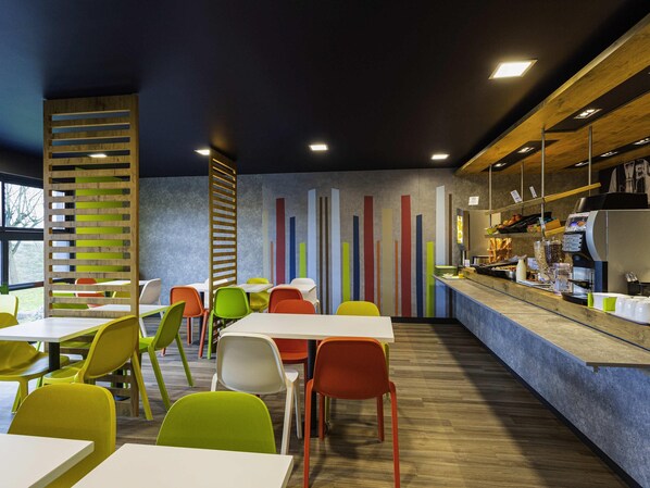 A modern cafe with colorful chairs, a bar area, and a counter with coffee-making equipment. - ibis budget Angoulême Nord (Champniers)