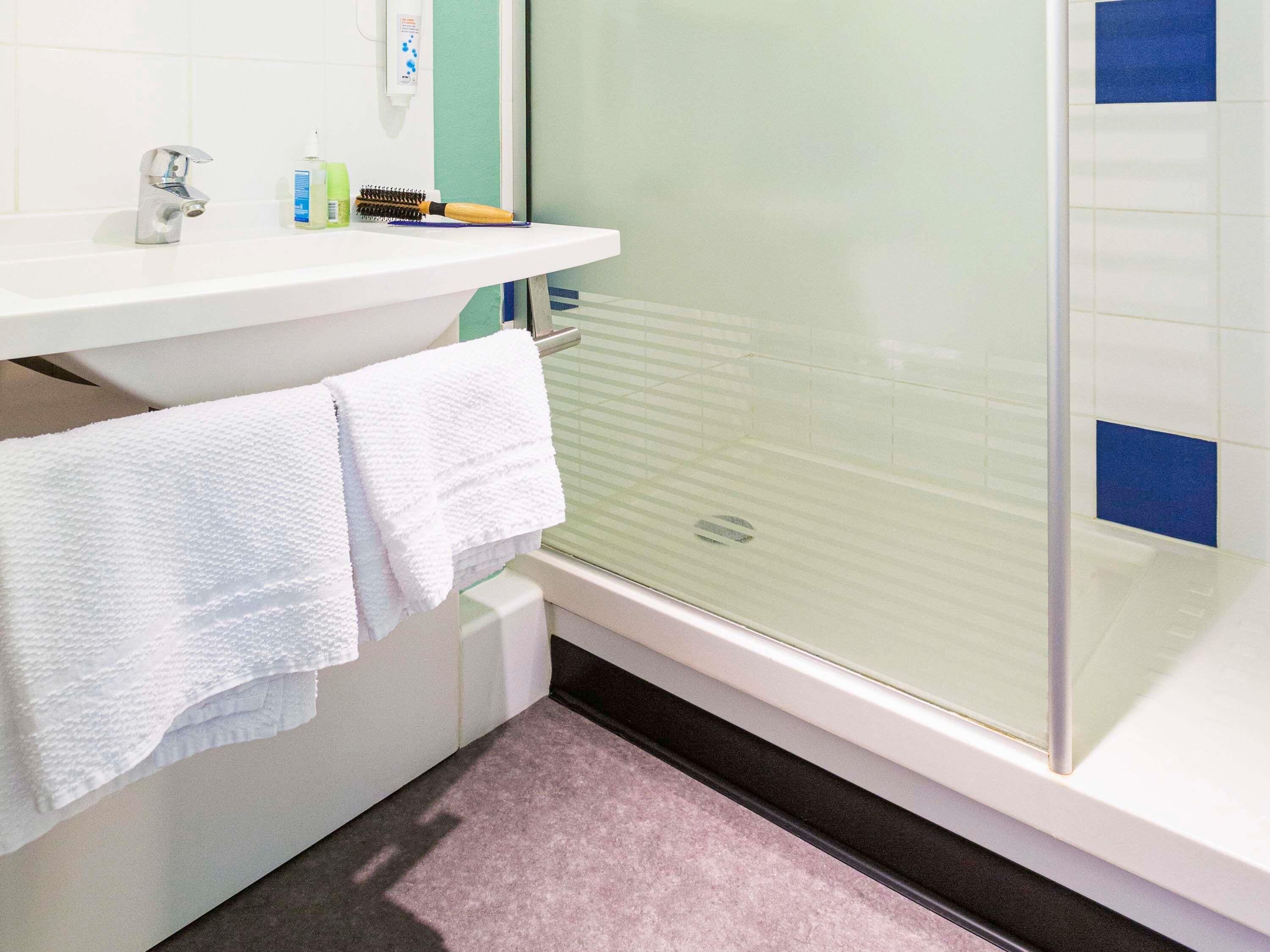 Un baño con lavamanos blanco, espejo, toallero y ducha con puerta de vidrio.