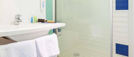 Un baño con lavamanos blanco, espejo, toallero y ducha con puerta de vidrio.