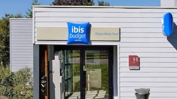 Entrada d'un hotel modern amb un cartell que indica 'ibis budget' i 'Angoulême Nord' com a localització.