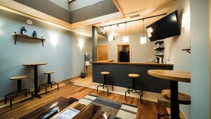 Un espace bar moderne avec des tabourets en bois, un comptoir et un téléviseur à écran plat fixé au mur.