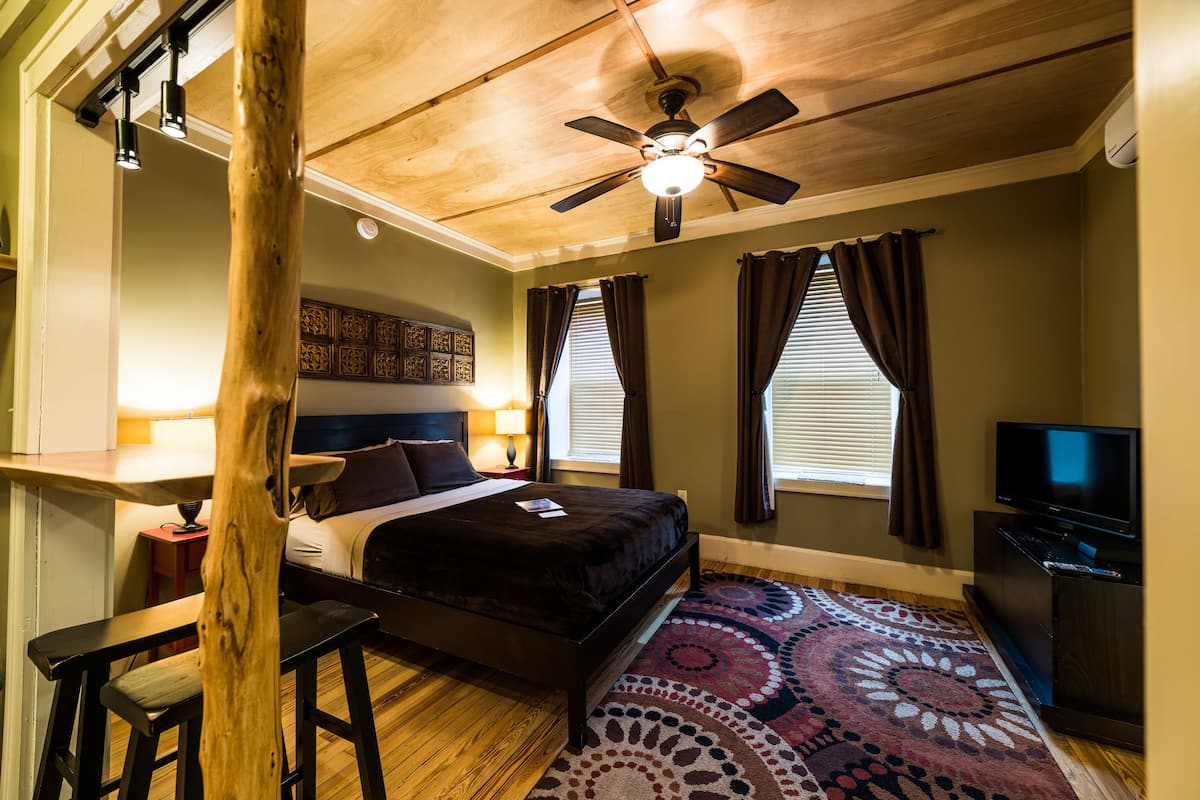 A bedroom with a bed, a ceiling fan, a TV, and a patterned rug.