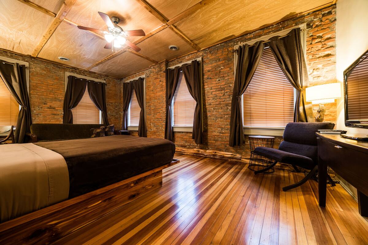 A room with a wooden floor, a bed, a desk, a chair, and a ceiling fan.