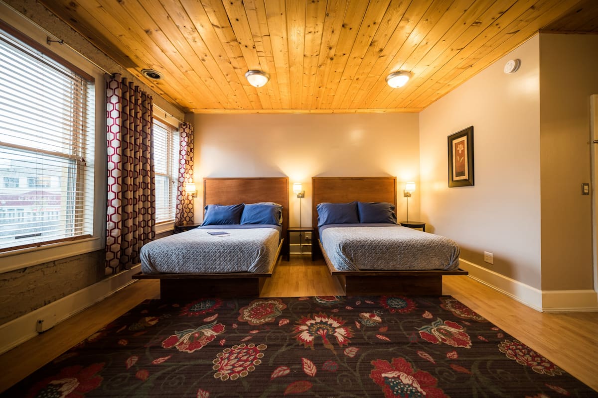 A room with two beds, wooden ceiling, and a patterned carpet.
