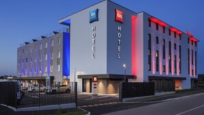 A modern hotel building with 'ibis budget' signage, a gated entrance, and a parking area. - ibis budget Sens (Sens)