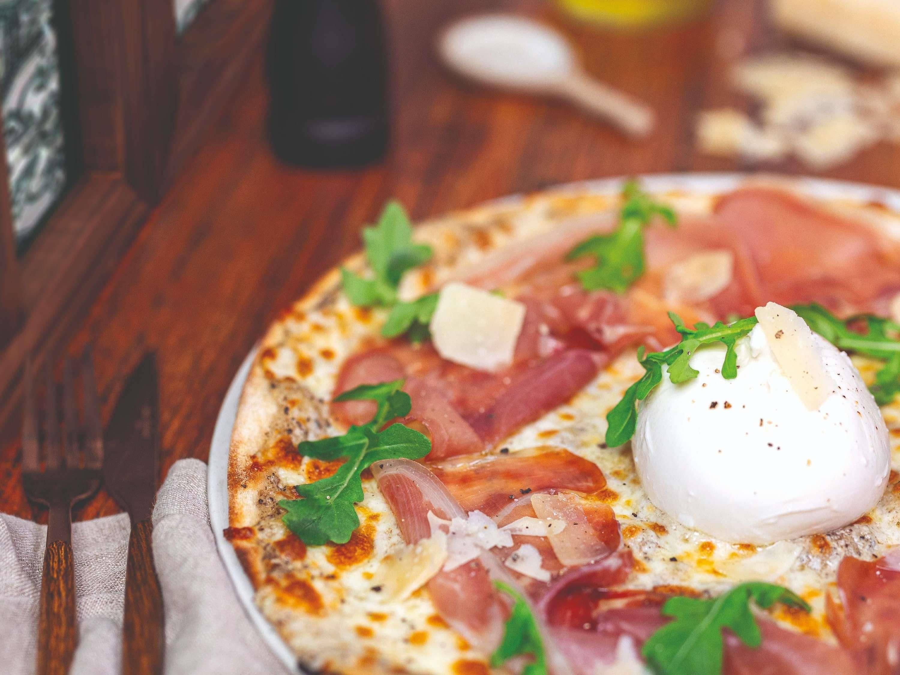 A pizza with toppings and a poached egg on a wooden table.