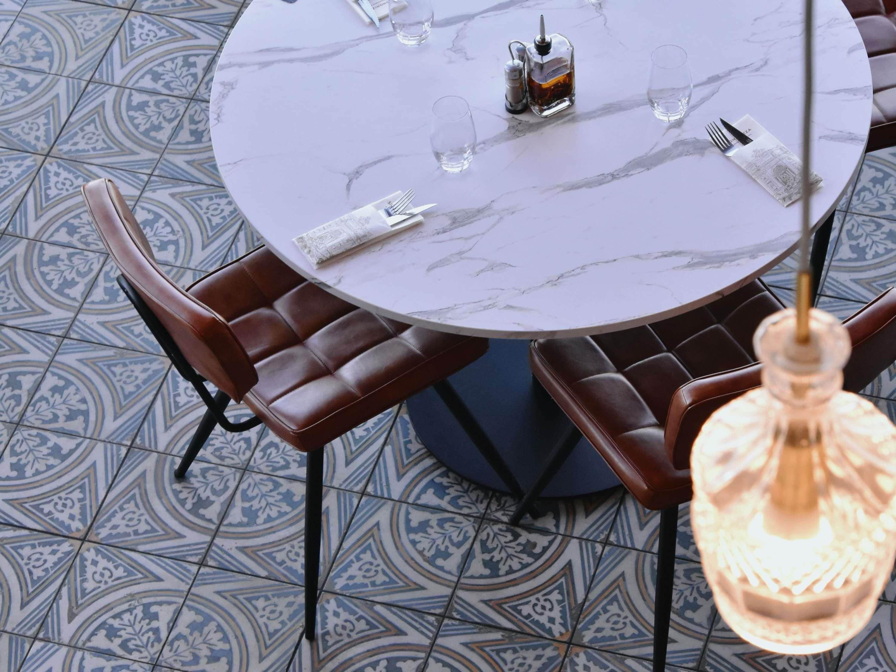 Une table ronde avec un plateau en marbre, entourée de fauteuils en cuir, et un luminaire suspendu.