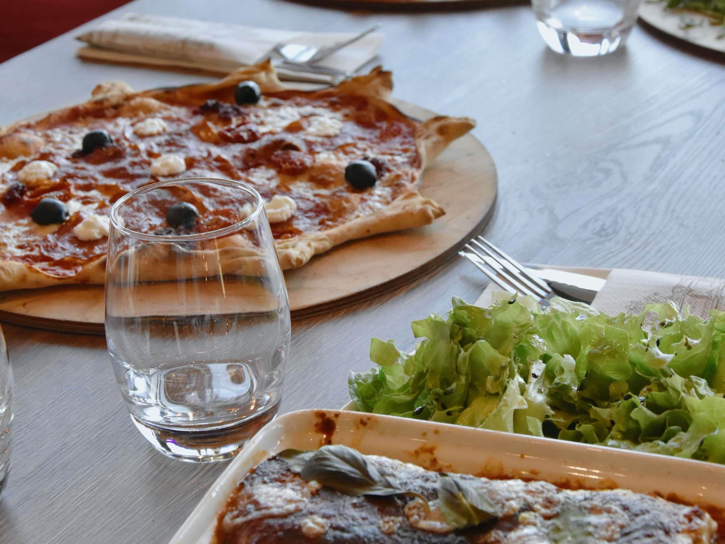 A dining table with a pizza, a glass of water, and a plate of salad.