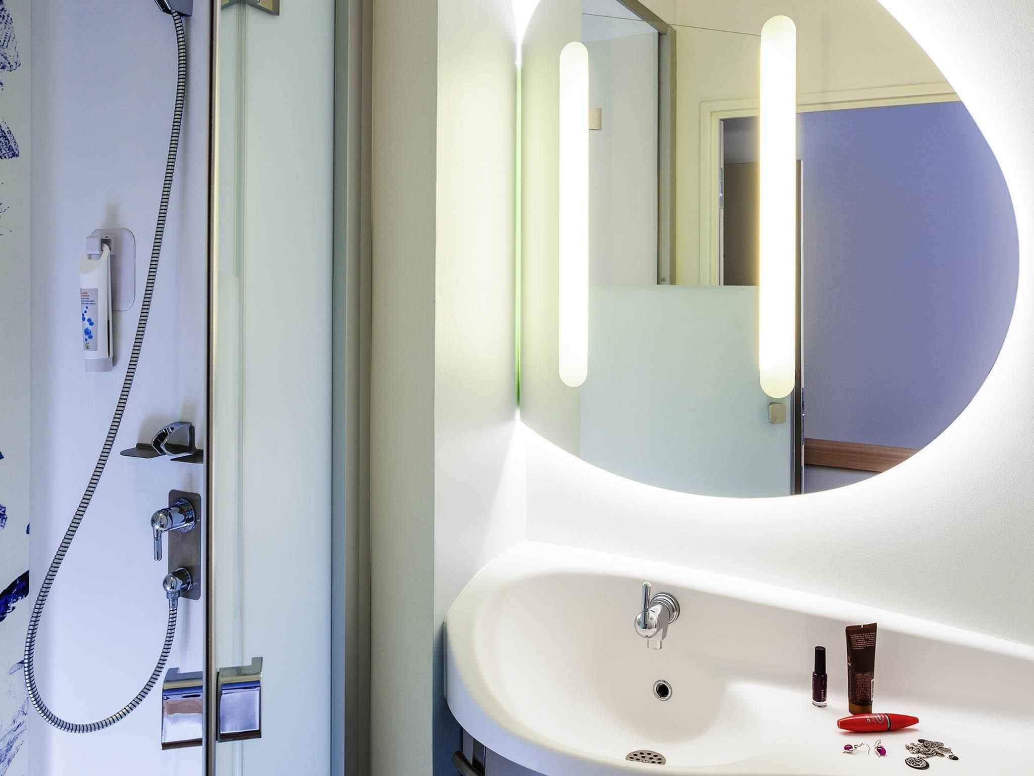 Een badkamer met een ronde spiegel, een wastafel en een douche met een handdouche.