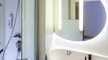 Een badkamer met een ronde spiegel, een wastafel en een douche met een handdouche.