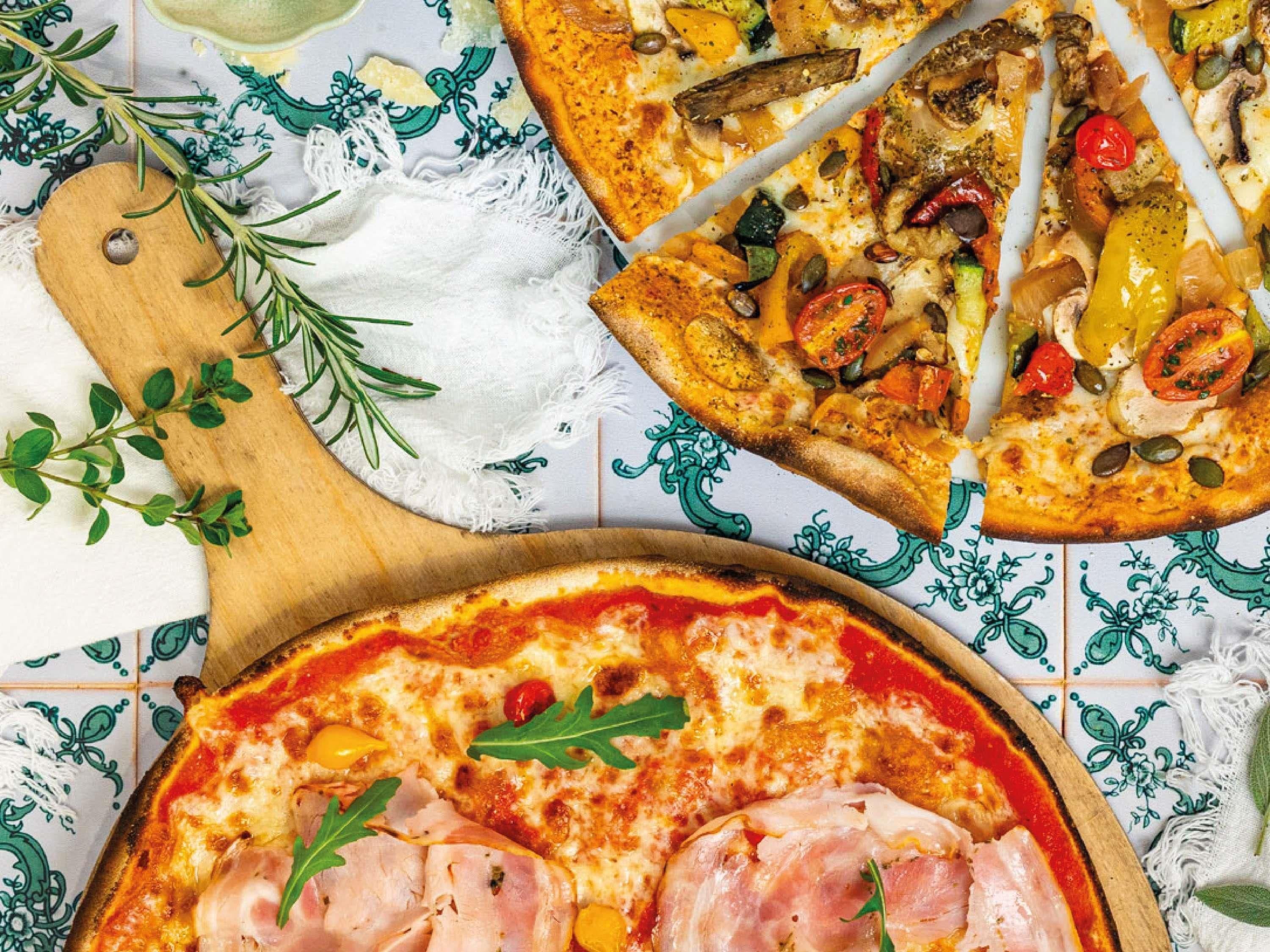 Pizza mit verschiedenen Belägen, ein Holzschneidebrett und ein Stoff mit Muster.