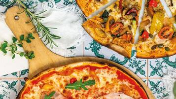 Pizza mit verschiedenen Belägen, ein Holzschneidebrett und ein Stoff mit Muster.