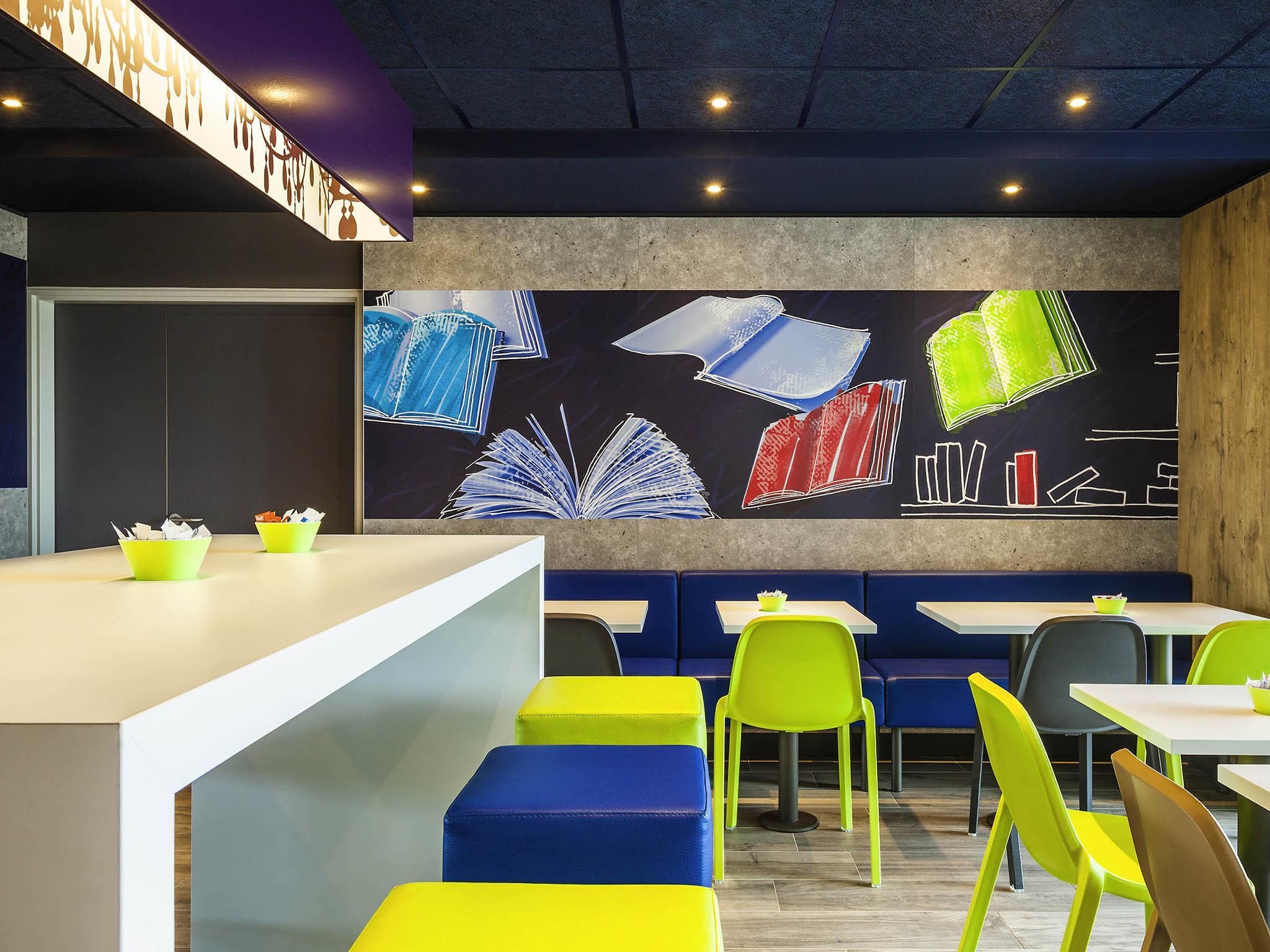 Un café moderno con asientos coloridos, una barra con menú y una pared decorada con ilustraciones de libros.