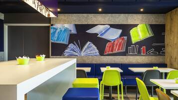Un café moderno con asientos coloridos, una barra con menú y una pared decorada con ilustraciones de libros.