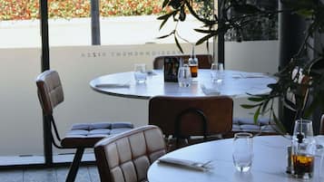 A restaurant with round tables and chairs, a menu stand, and a view of a garden.