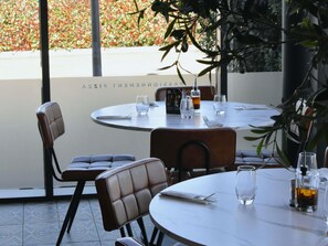 A restaurant with round tables and chairs, a menu stand, and a view of a garden. - ibis budget Sens (Sens)