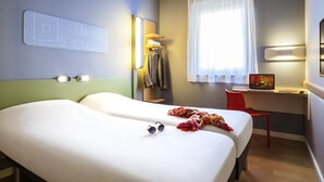 A hotel room with two beds, a desk with a laptop, a chair, a coat rack, and a window with curtains. - ibis budget Sens (Sens)