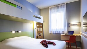 Habitación de hotel con cama, escritorio con computadora portátil, silla, escalera y televisor.
