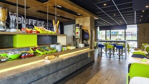 Un café moderno con un mostrador que exhibe alimentos, una máquina de café y una zona de estar con mesas y sillas.