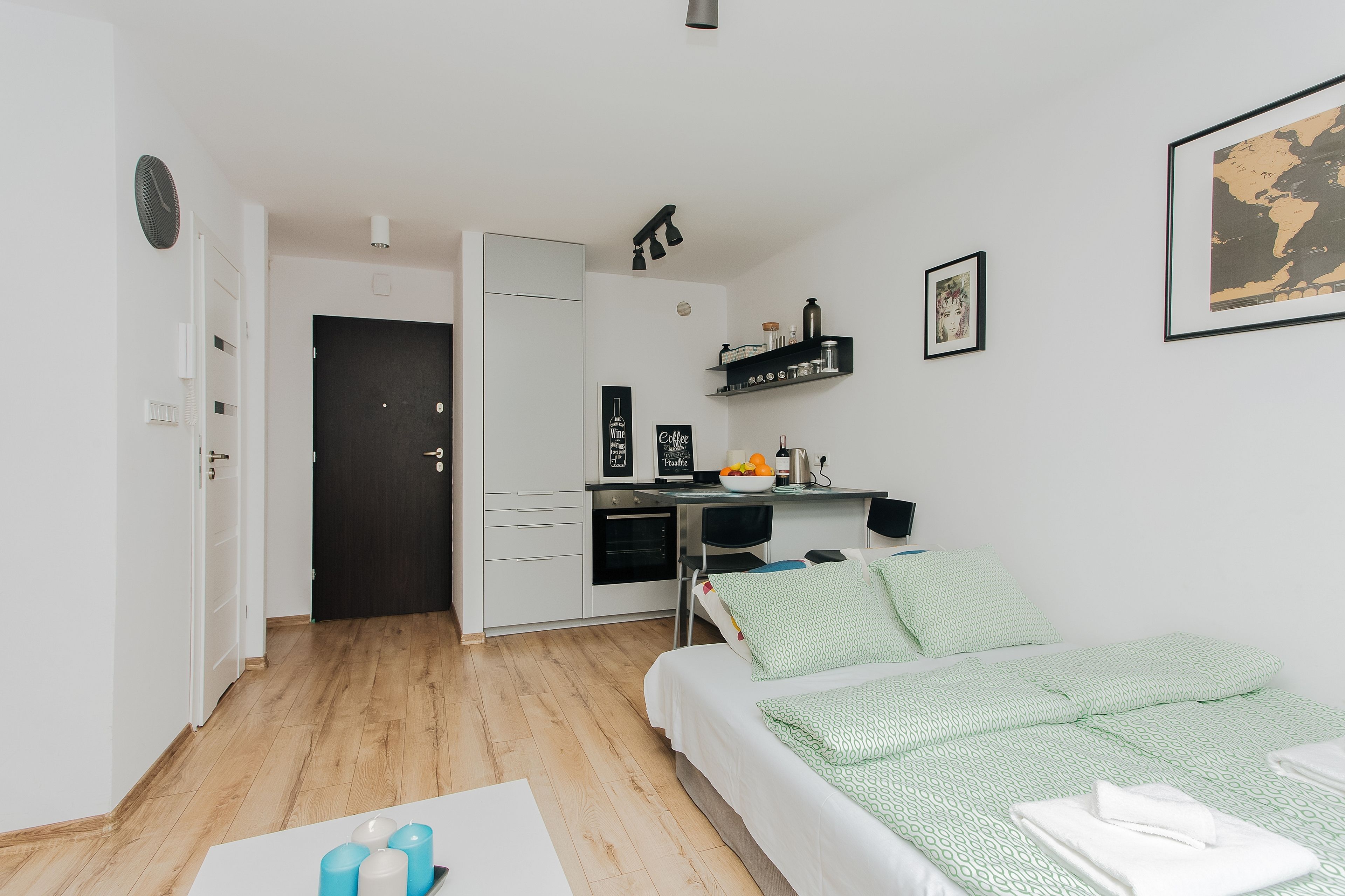 A compact, modern room with a bed, a desk, and a kitchenette.