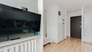 En moderne stue med et fladskærms-TV monteret på en hvid væg, en radiator nedenunder og trægulv.