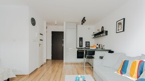 En moderne stue med sofa, sofabord med stearinlys, et tekøkken med køleskab og et spisebord.