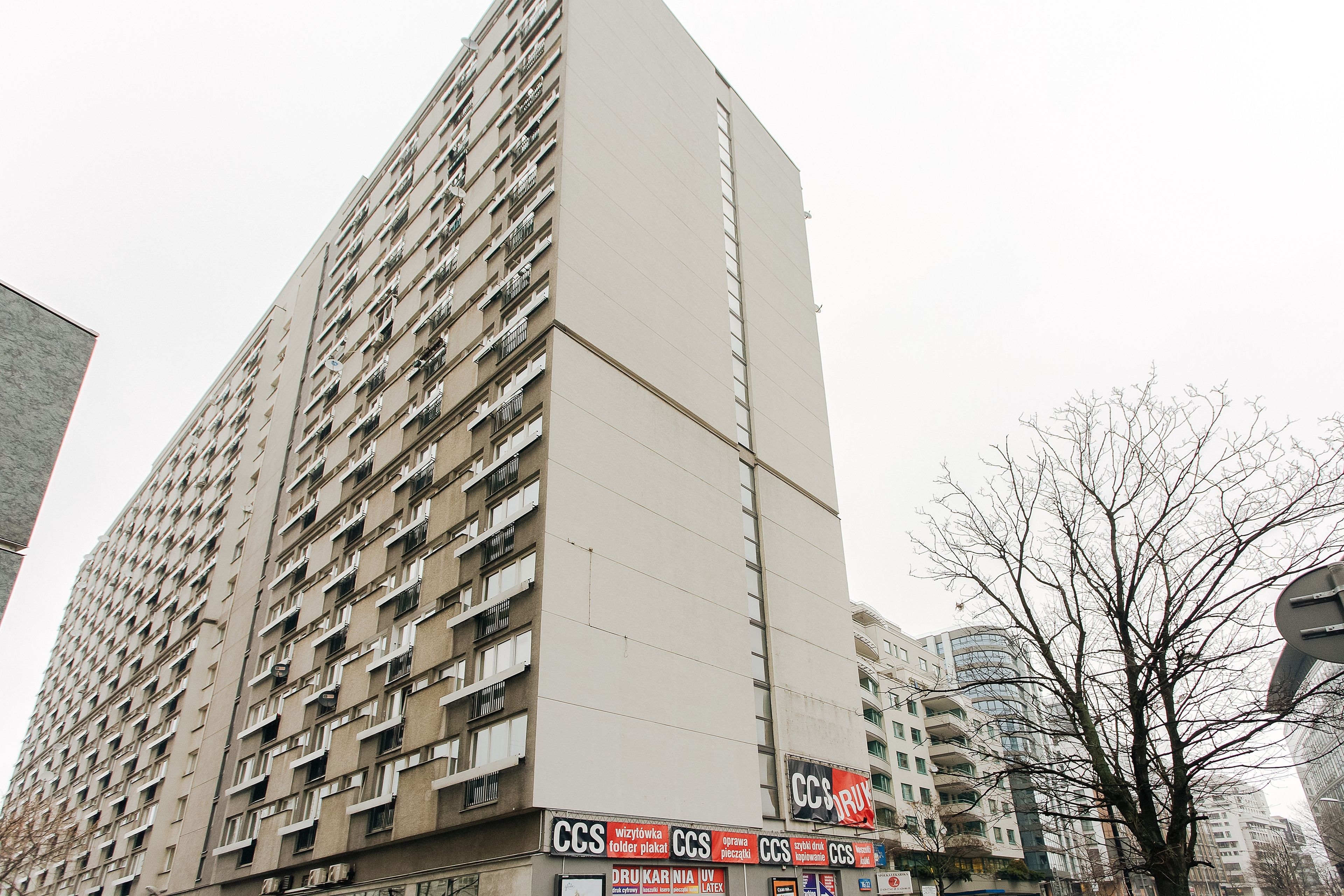 A tall residential building with multiple balconies and a storefront at the ground level.