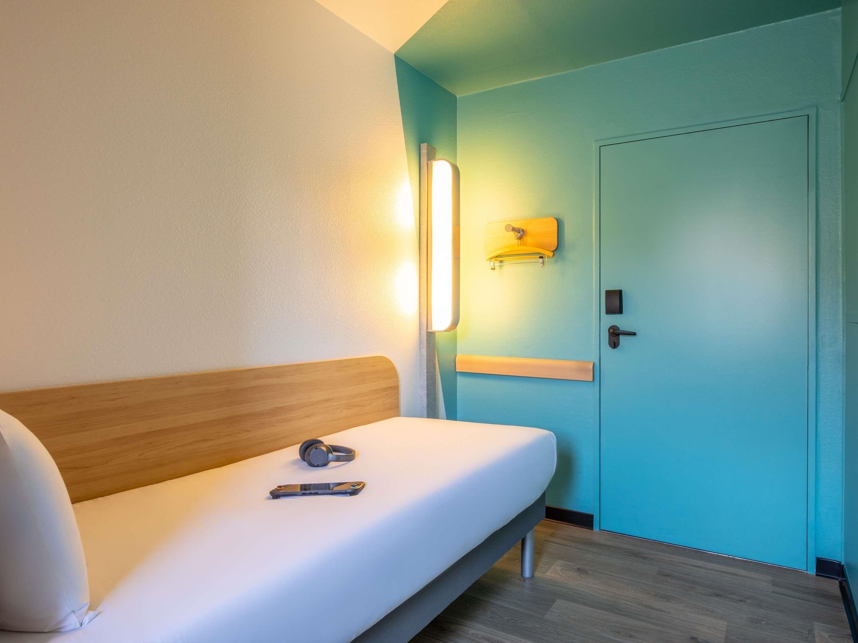 Una cama individual con cabecera de madera, una mesita de noche, una lámpara de pared y una puerta con manija.