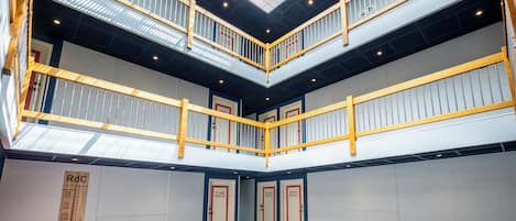 A multi-level atrium with a patterned floor, a central staircase, and a series of doors with numbers.