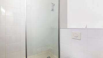 Une salle de bain avec des carreaux blancs, une douche en verre et des toilettes.