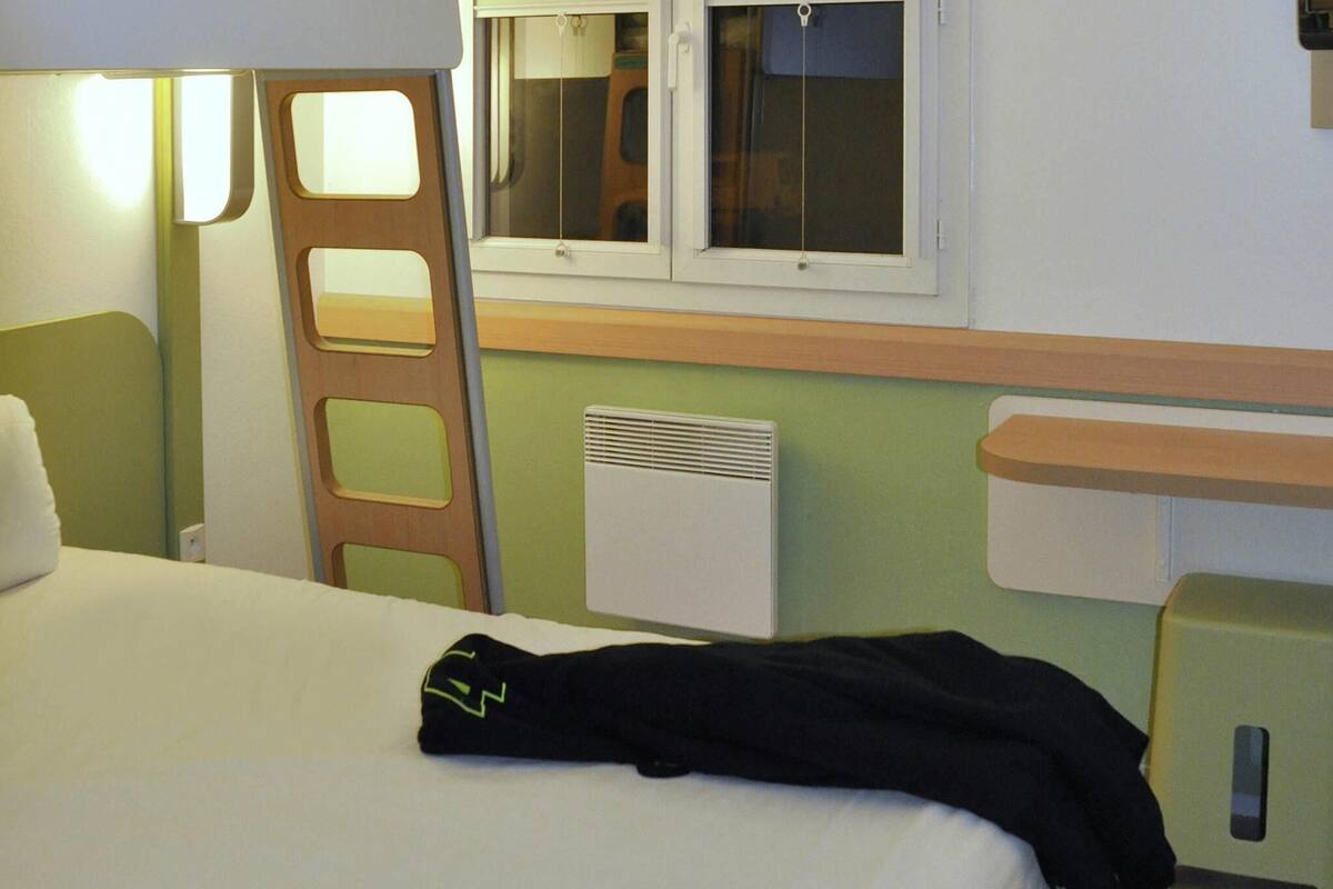 A hotel room with a bed, a window, a heater, and a bedside table.